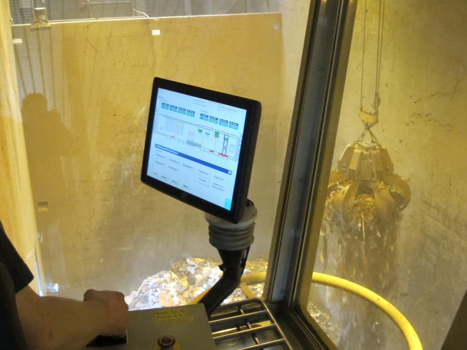 Blick aus der Krankabine mit einem Monitor auf den Greifarm mit Abfall