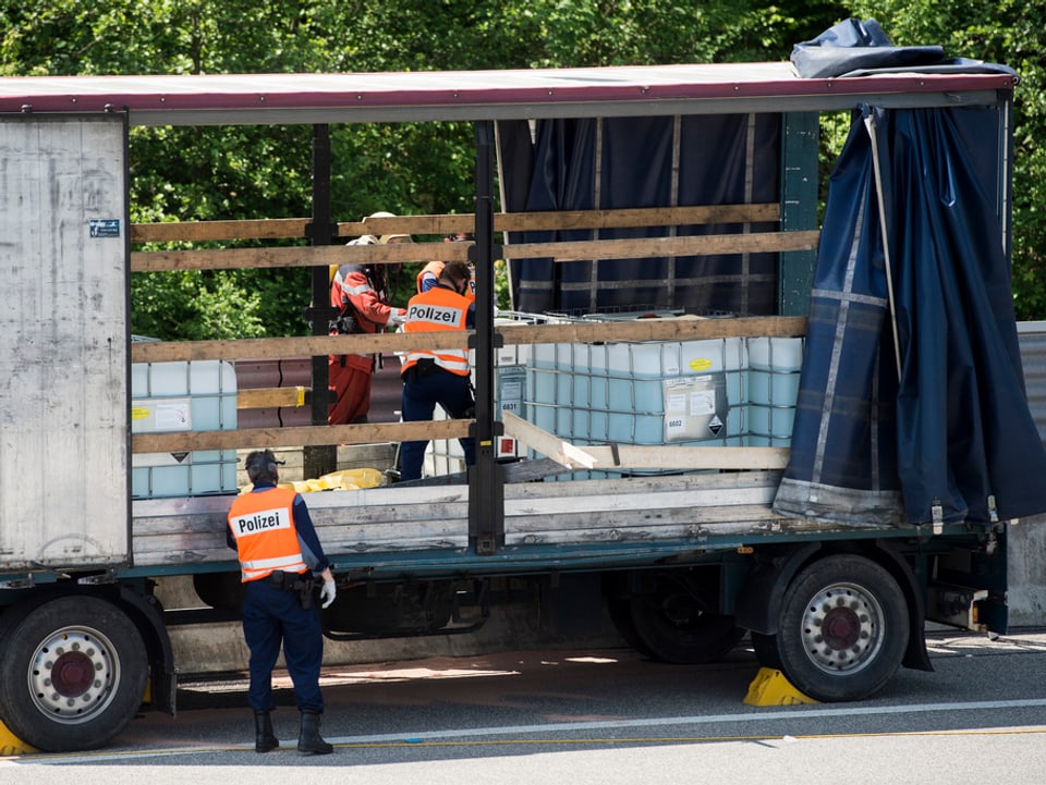 Polizisten mit Gasmasken inspizieren Plastiktanks mit Flüssigkeit auf der Ladefläche eines Lastwagens