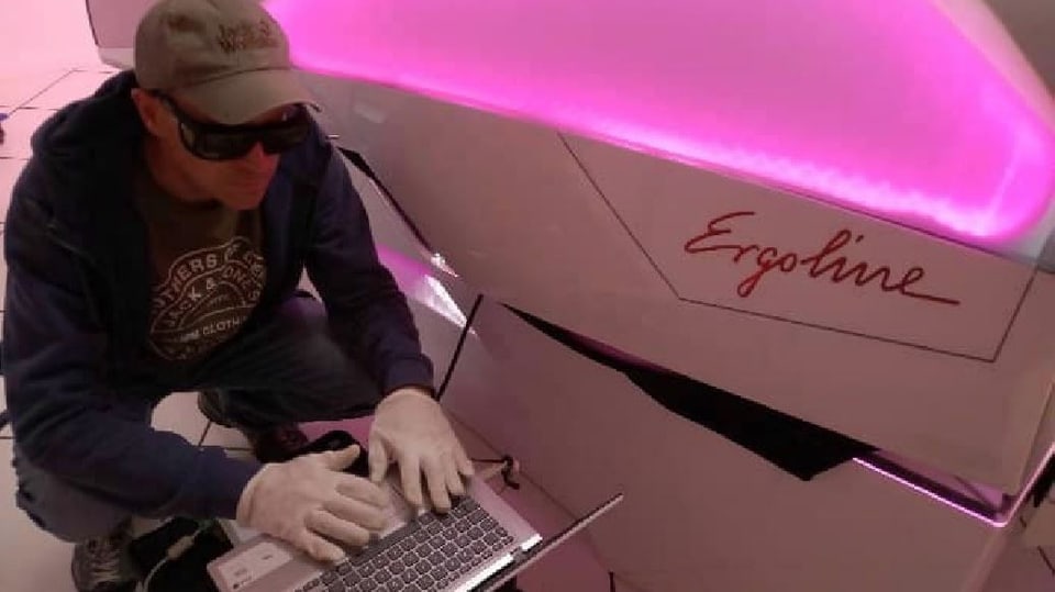 Mann mit Kappe und dicker Sonnenbrille mit Computer neben einem Solarium