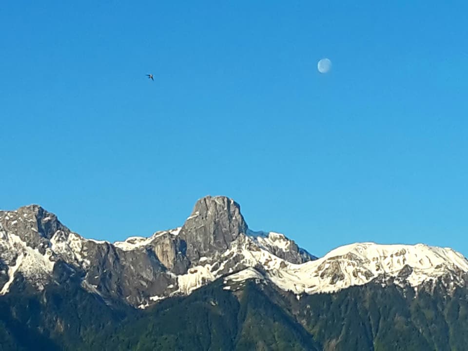 Berge, blauer Himmel und der Mond als kleiner Punkt.