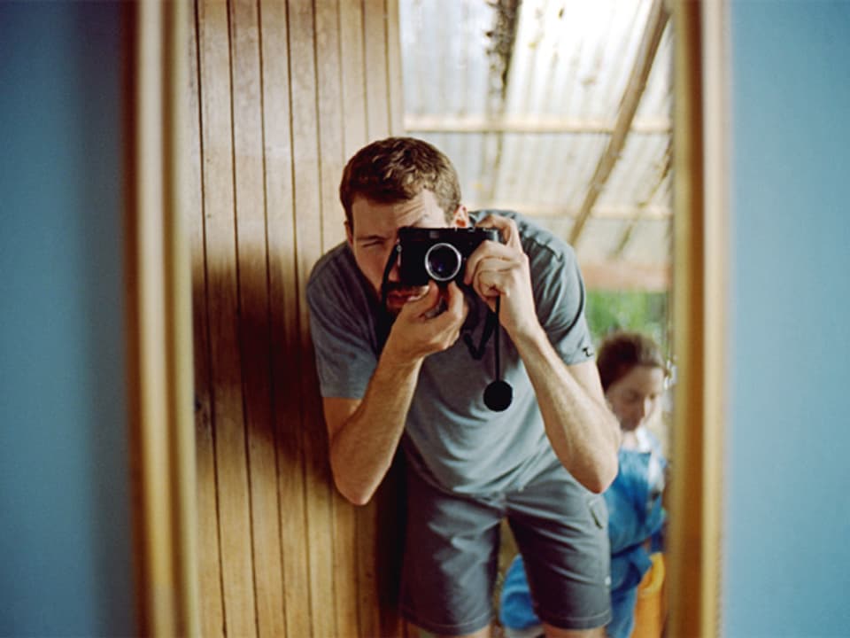 Ein Mann in einem Türrahmen mit einer Kamera vor dem Gesicht.