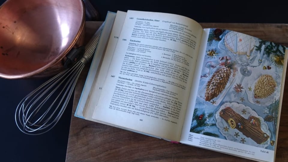 Farbfoto altes Kochbuch mit Kuchenillustrationen, links Kupferschüssel und Schwingbesen