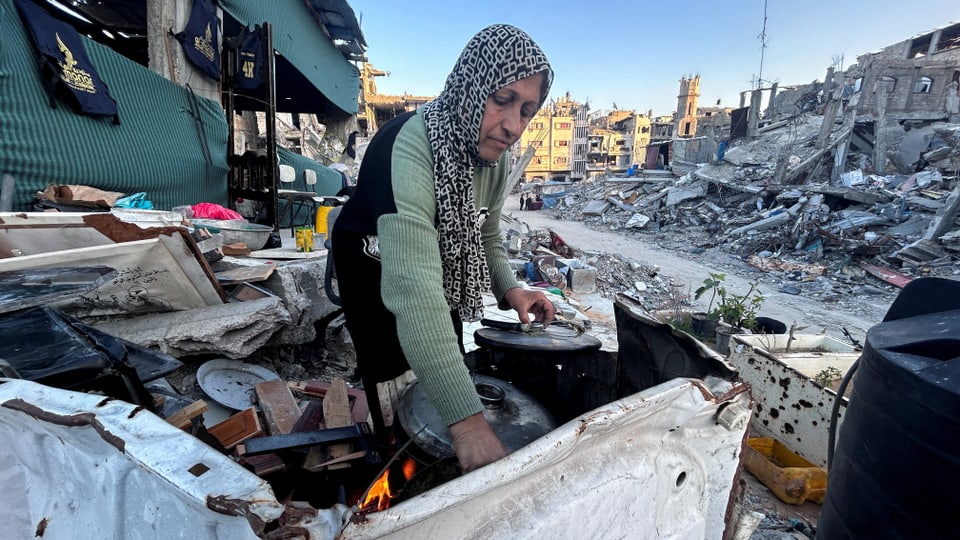Symbolbild: Eine Frau kocht in den Trümmern zerbombter Häuser etwas zu essen.