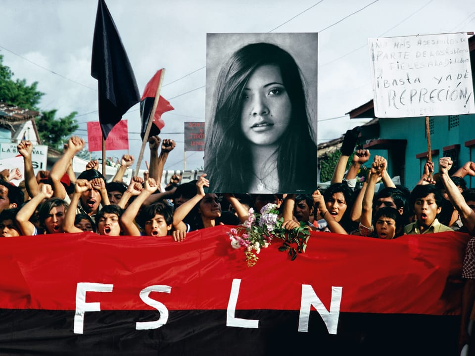 Zahlreiche Jugendliche geben mit Plakaten und erhobenen Fäusten ihrem Unmut Luft, quer vor ihnen her tragen sie ein meterlanges rotes Stofftuch mit der Aufschrift FSLN.