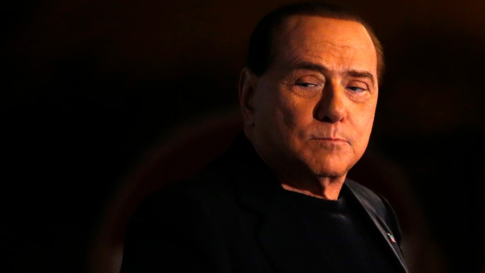 Nur Berlusconis Gesicht ist gut sichtbar, beleuchtet in der Dunkelheit.