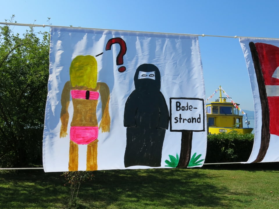 Ein Stück Stoff, daruf gemalt sind eine Frau im Bikinu und eine im Burkini.