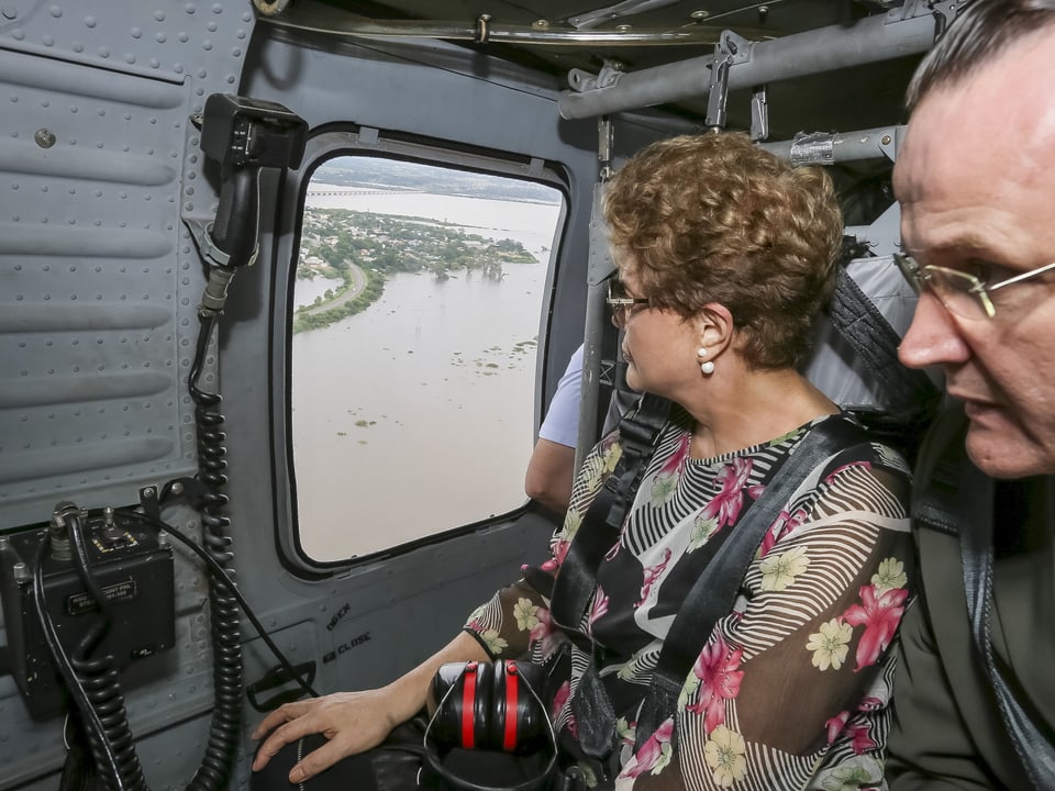 Dilma Roussef, Präsidentin von Brasilien, mit einem anderen Mann im Vordergrund, schaut aus einem geschlossenen Helikopter.