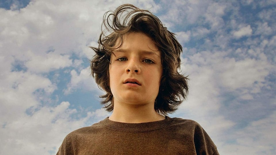 Ein Junge vor einem Wolkenhimmel.