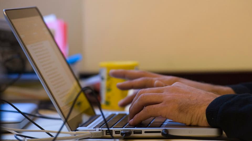 Ein Mann schreibt auf einem Laptop.