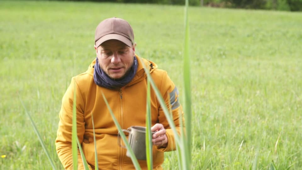 Mann mit Mütze und Kapuzenpullover mit einer Tasse in der Hand draussen.