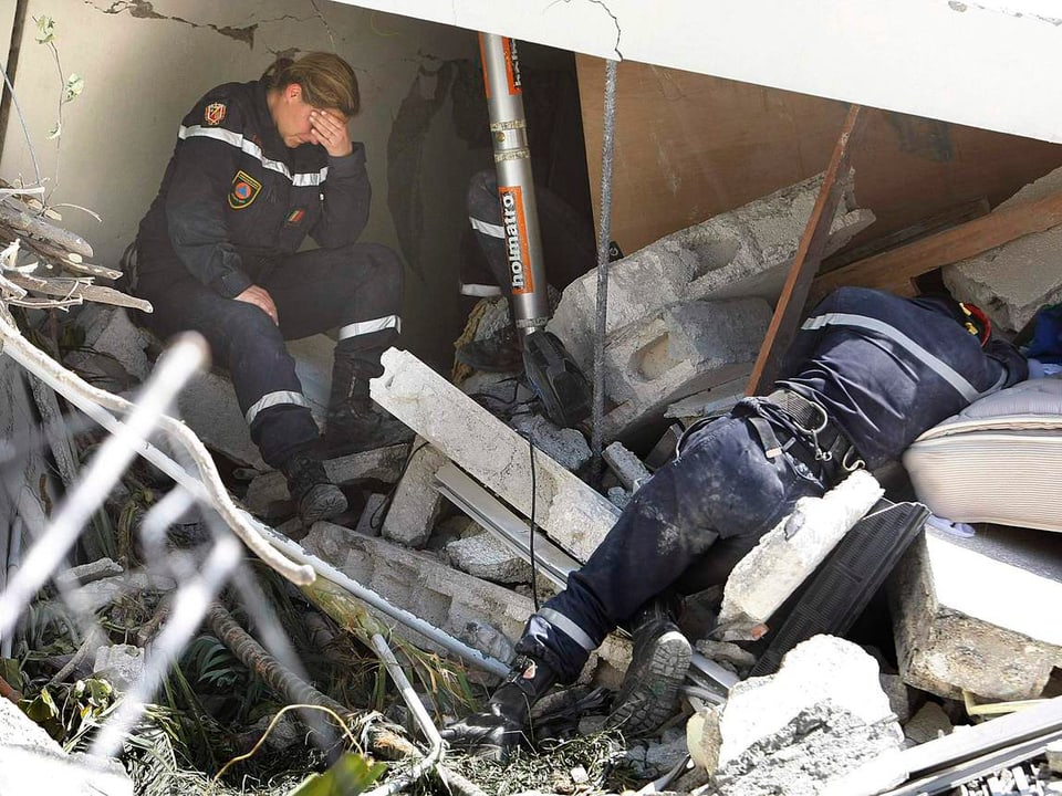 Eine Mitarbeiterin der Rettungskräfte sitzt erschöpft auf den Trümmern eines Hauses, während ihr Kollge weiter nach Opfern sucht.