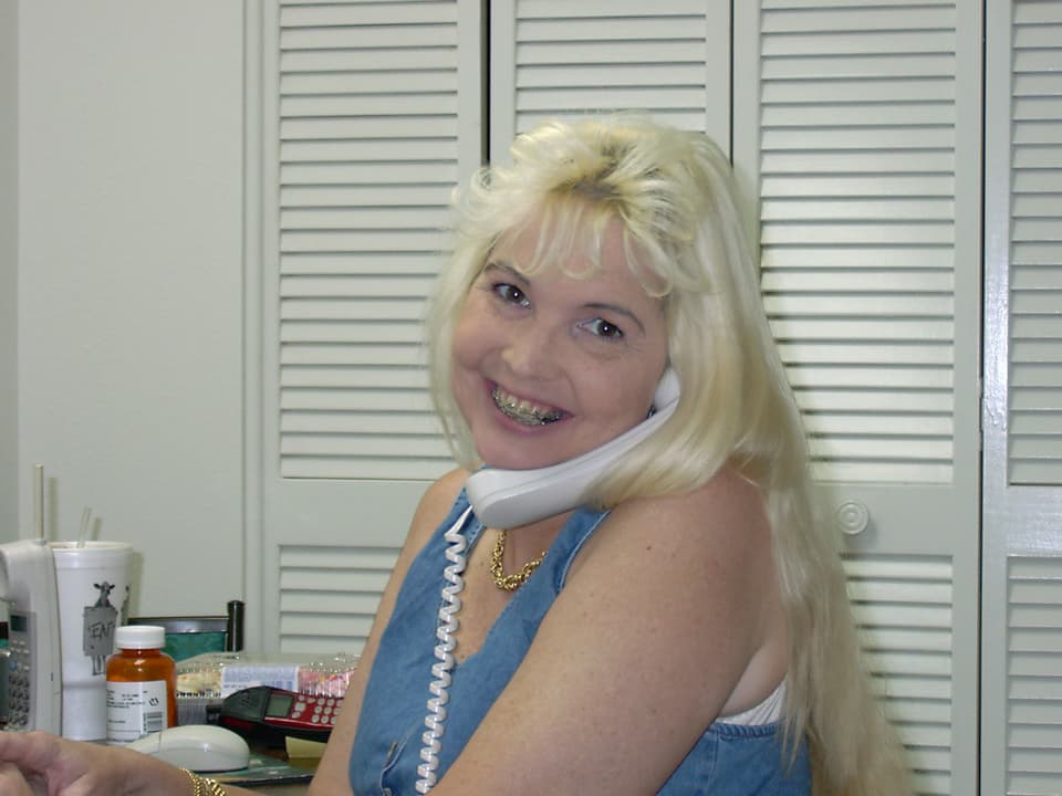 Eine Frau mit einer Zahnspange klemmt sich einen Telefonhörer zwischen Backe und Schulter.