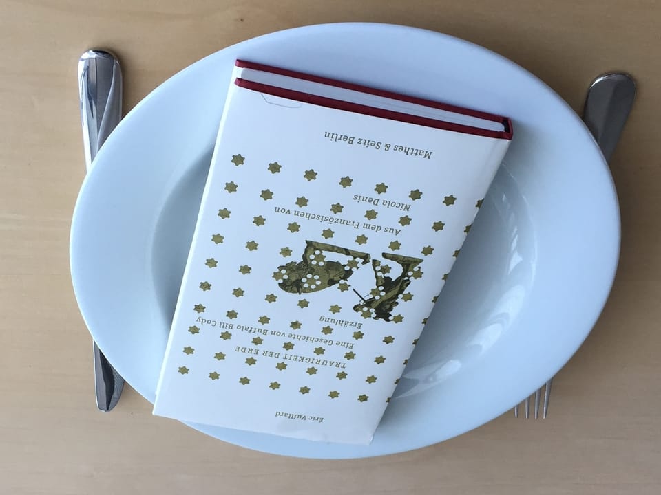 Das Buch «Traurigkeit der Erde» von Éric Vuillard liegt auf einem weissen Teller. Messer und Gabel liegt daneben. 