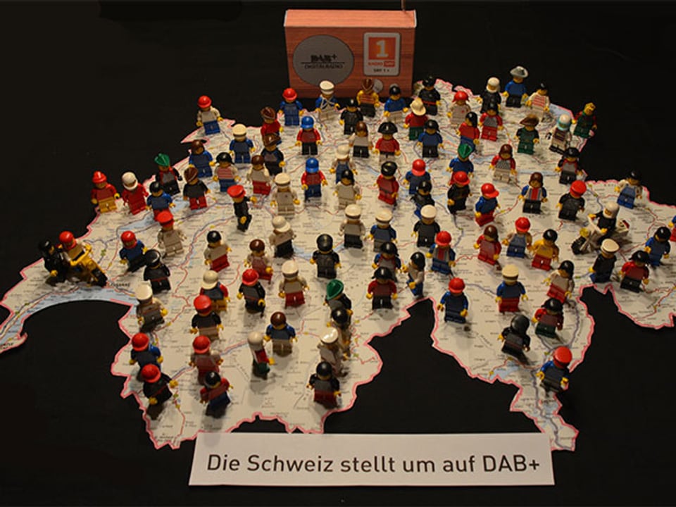 Bild von einer augedruckten Karte der Schweiz mit Lego Menschen und Unterschrift: «Die Schweiz stellt um auf DAB+».