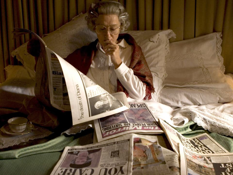 Helen Mirren als Queen mit einer Tasse Tee im Bett, vor sich verschiedene Zeitungen.
