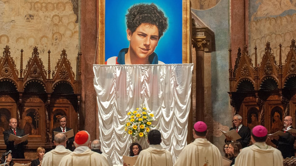 Clergy celebrate mass in front of a large portrait of a young man.