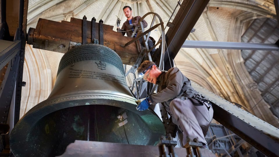 Männer arbeiten an einer grossen Kirchenglocke, die in einem Turm hängt.