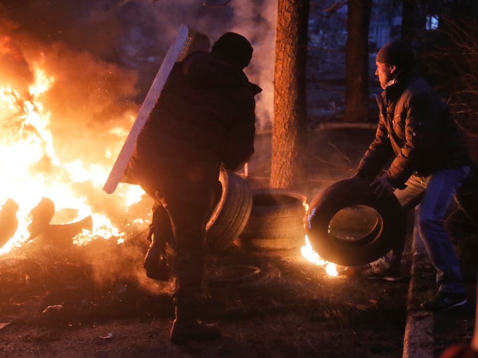 Zwei schwarz gekleidete Aktivisten werfen Reifen in ein Feuer: Der Rauch soll die Sicht der Scharfschützen auf die Protestierenden erschweren. 