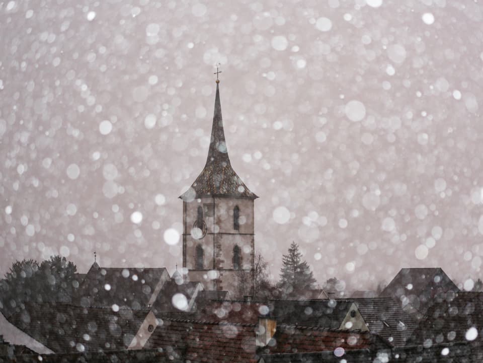 Schneefall mit Sicht auf eine Kirche.