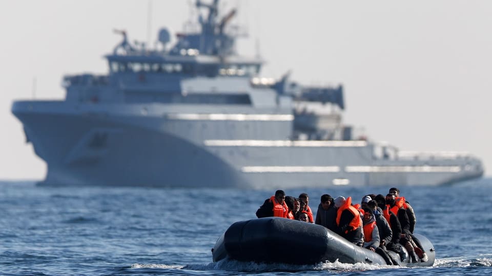 Im Vordergund ein Schlauchboot mit Migranten, im Hintergrund ein Hochseeschiff