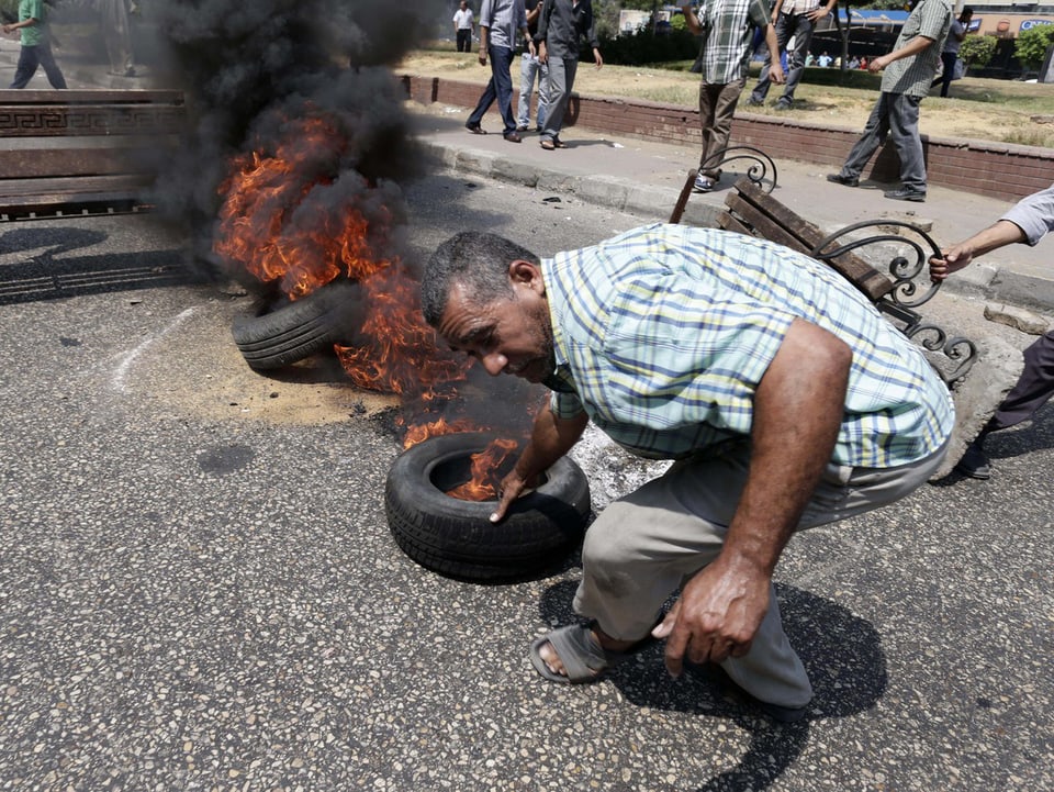 Mann zieht brennenden Reifen auf die Strasse.