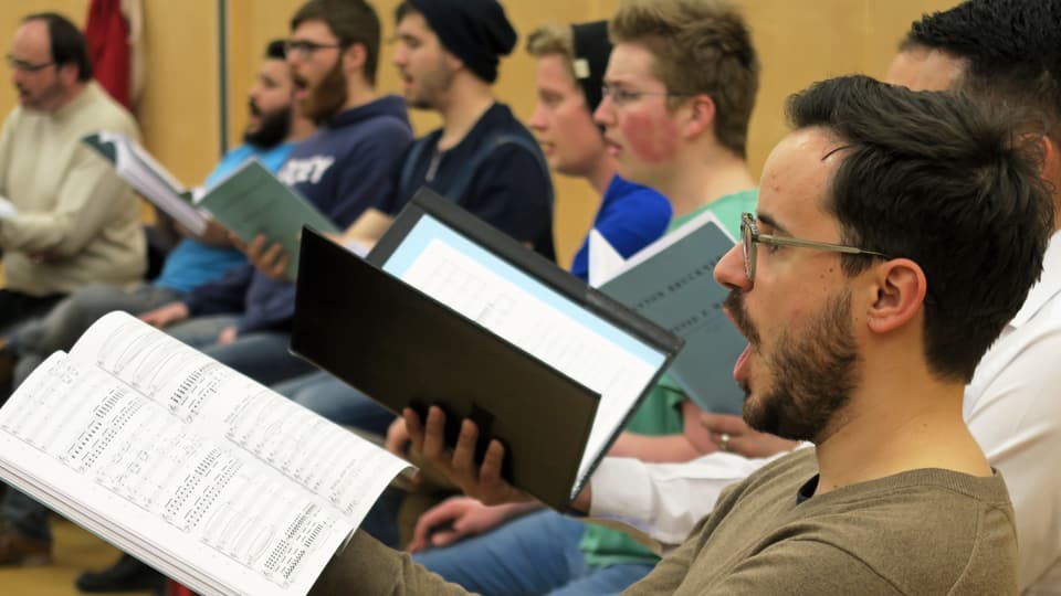 Ein Chor bei der Probe: Männer mit einem Notenblatt in der Hand singen. 