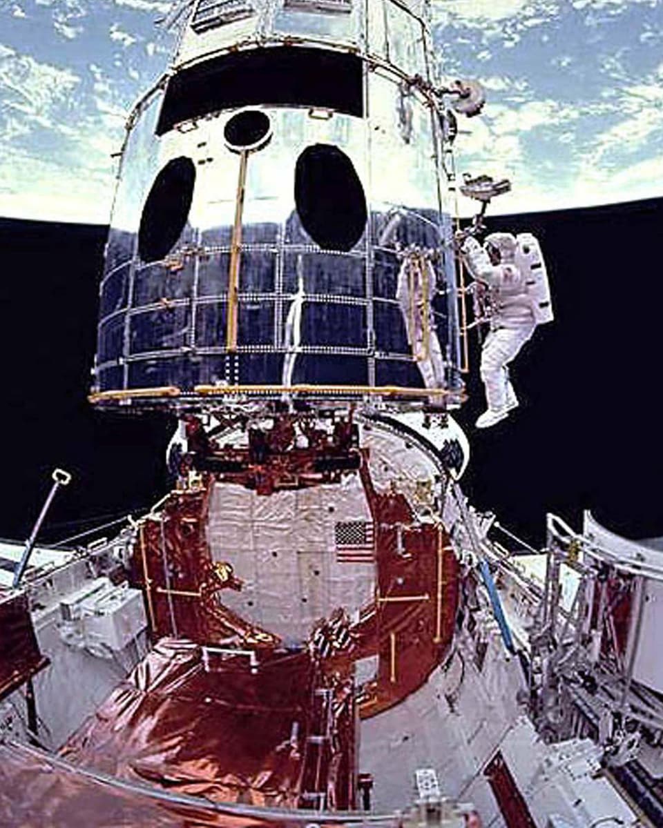 Ein Astronaut arbeitet am Teleskop. IM Hintergrund die Erde.