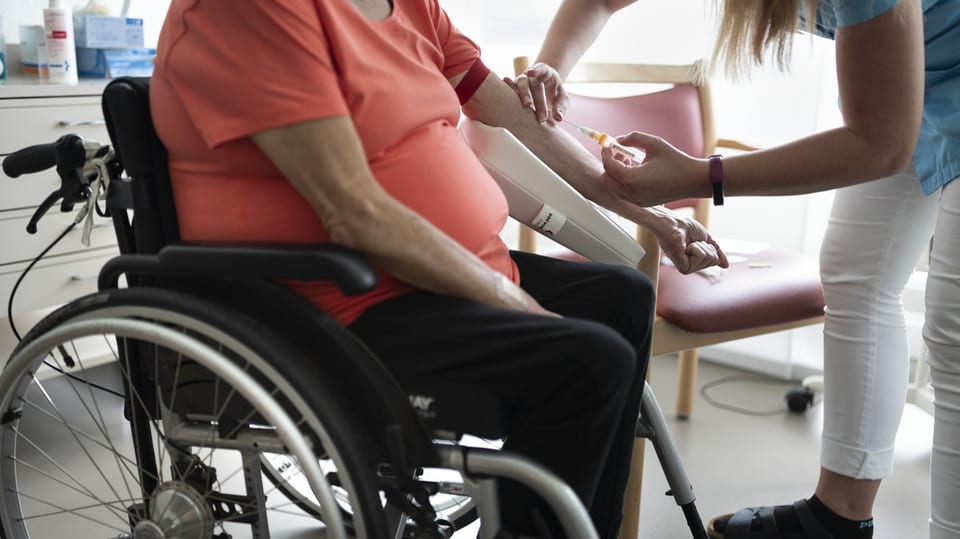 Eine Praxisangestellte nimmt einer älteren Person im Rollstuhl Blut ab.