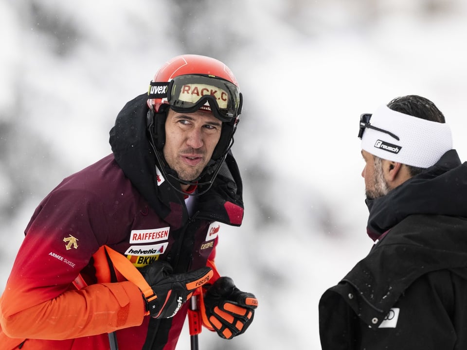 Zwei Männer im Gespräch im Schnee, einer in Skiausrüstung und Helm