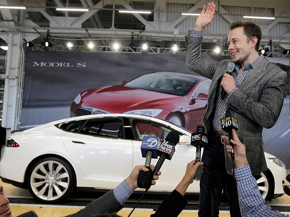 Elon Musk, dahinter steht ein Tesla-Elektrosportwagen