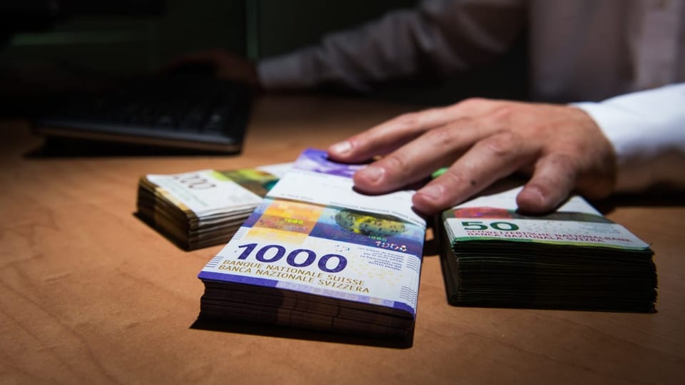 Hand auf mehreren Bündeln Banknoten, hinten Schatten