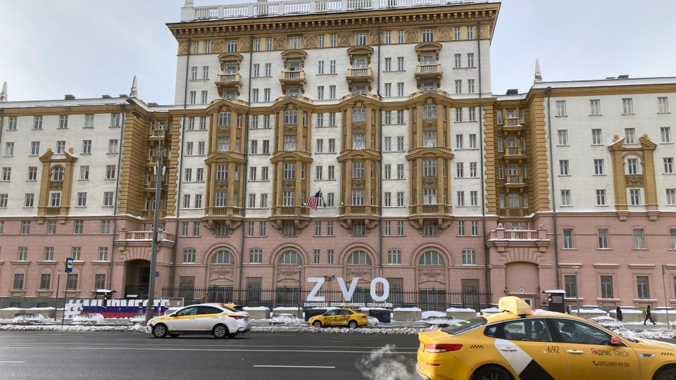 A large, white and pink building with a multi-lane road in front of it.  White letters in front of the building: 