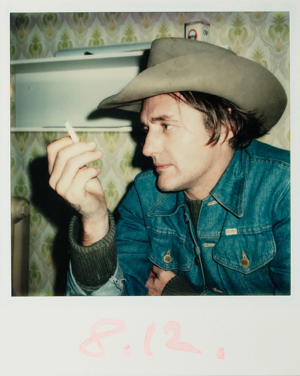 Ein Mann mit Cowboy-Hut und Jeans-Jacke hält eine Zigarette in der Hand.