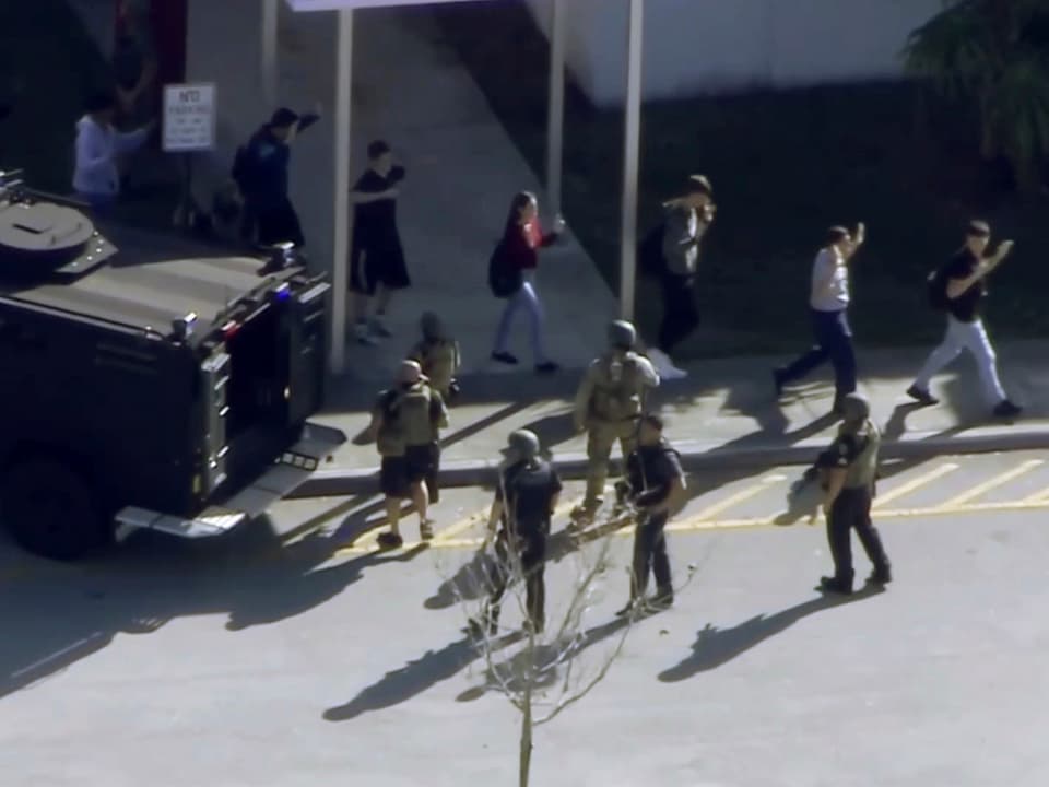 Schüler verlassen die Schule mit erhobenen Händen, Sicherheitskräfte stehen daneben