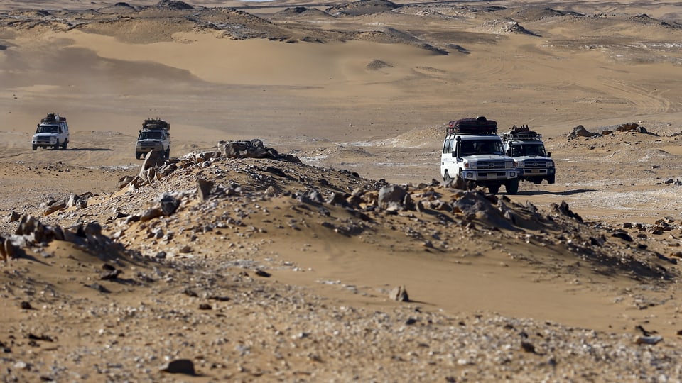 Vier Geländefahrzeuge mit Dachgepäck in der Wüste.