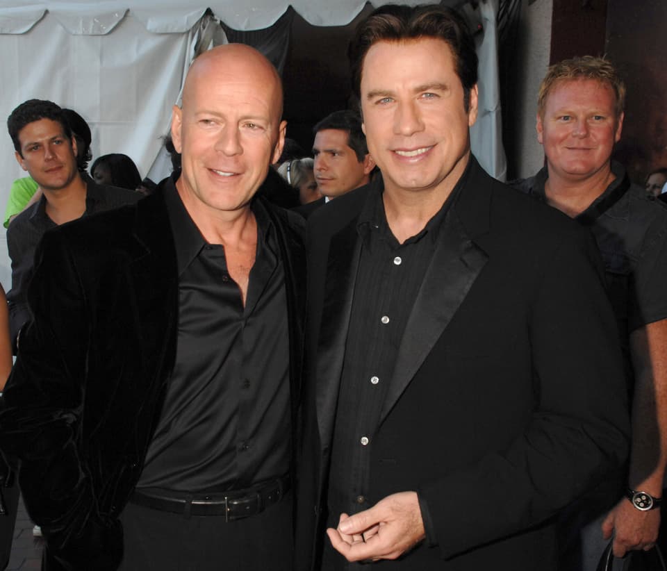 Bruce Willis und John Travolta posieren Arm in Arm.