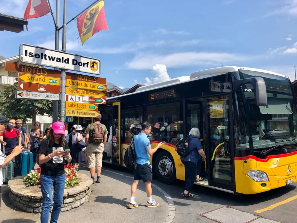 Asiatische Touristinnen und Touristen mit Rollkoffern stehen neben einem gelben Postauto