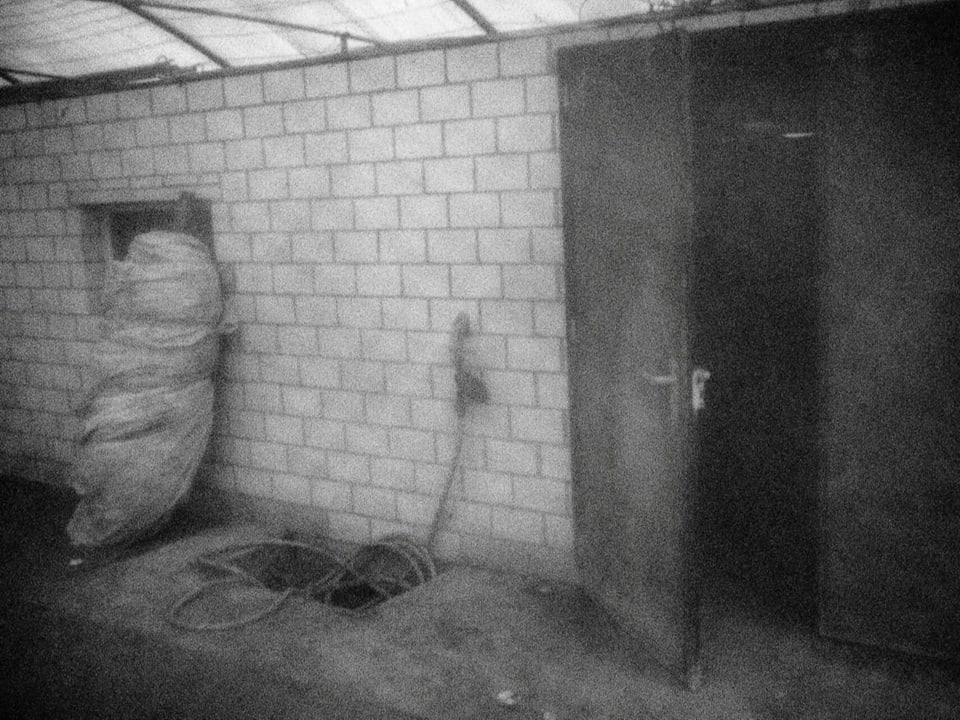 Eine verschwommene Aufnahme eines Abstellraums, der mit weissen Backsteinen gedeckt ist. Eine Tür steht halb offen.