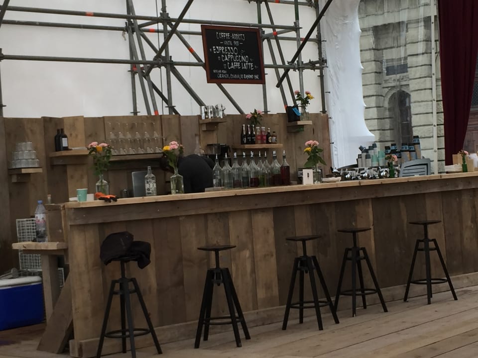 Eine Bar aus Holz, davor stehen vier Hocker, darauf Gläser.