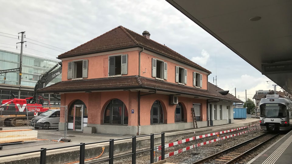 Der WSB-Bahnhof in Aarau. Links ein Bagger, der das Gebäude abreisst, rechts ein Zug an einem Perron.