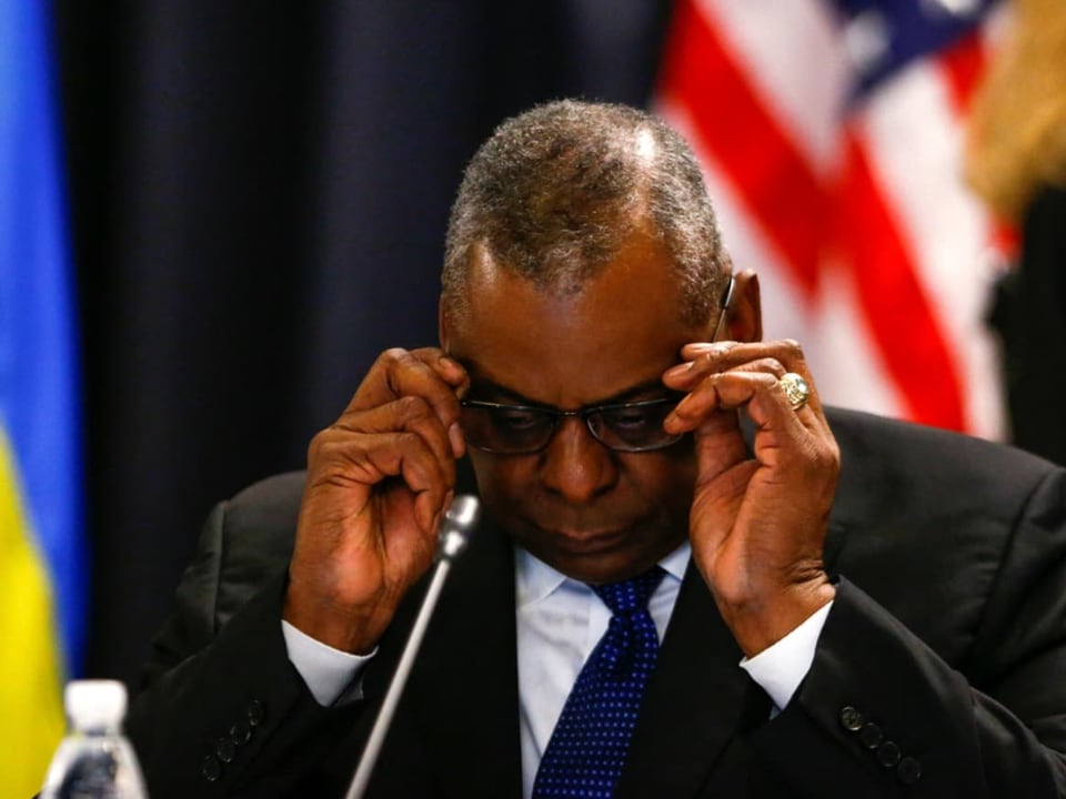 US-Verteidigungsminister Lloyd Austin legt die Brille ab. Er sitzt auf einem Podium.