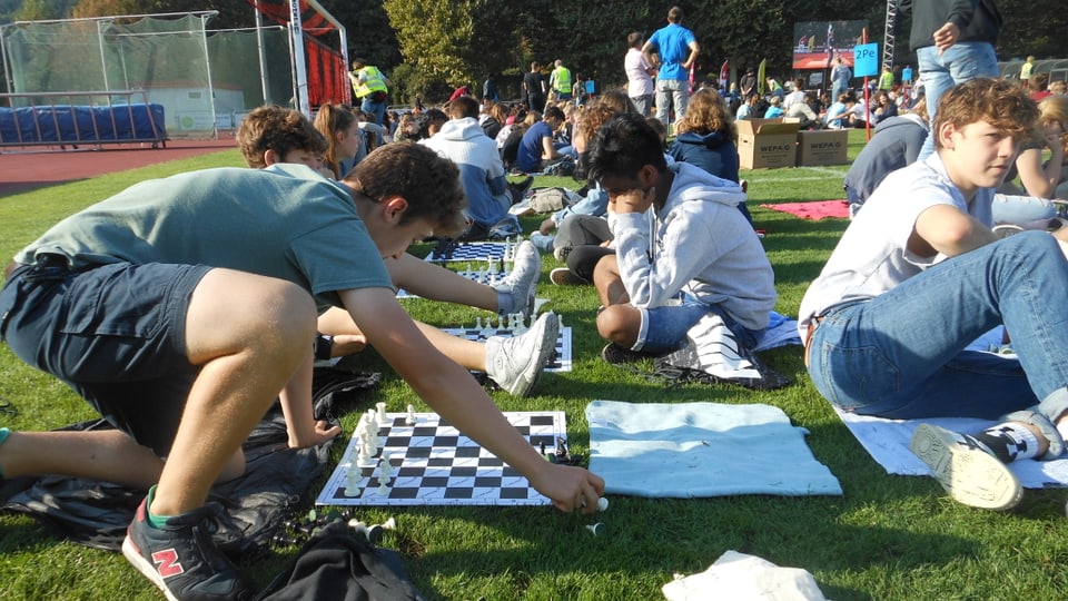 Man sieht Jugendliche, die vor Schachbrettern sitzen 