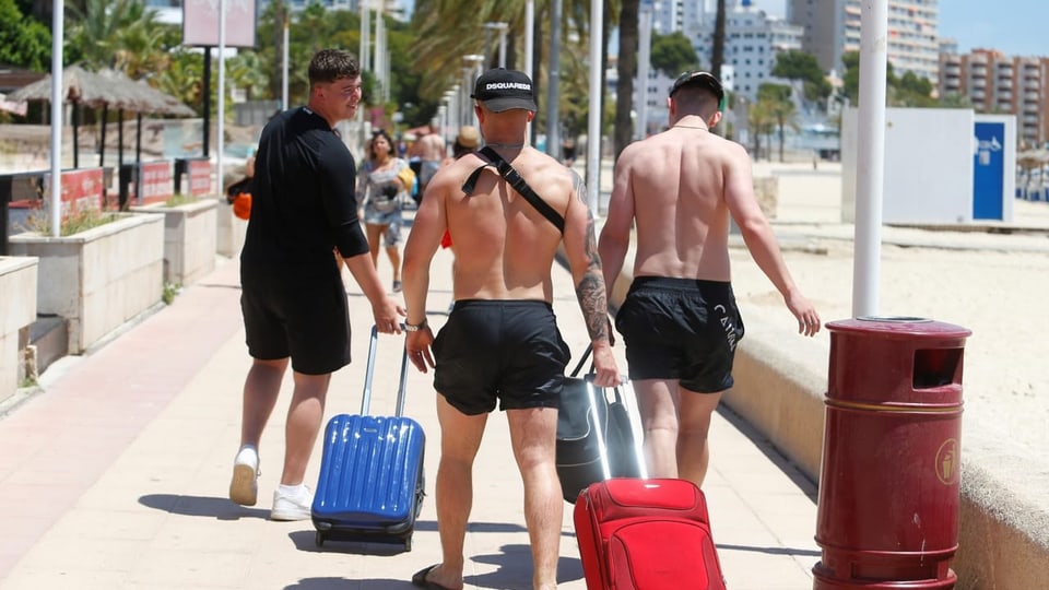 Drei Touristen mit Rollkoffer auf der Strandpromenade.