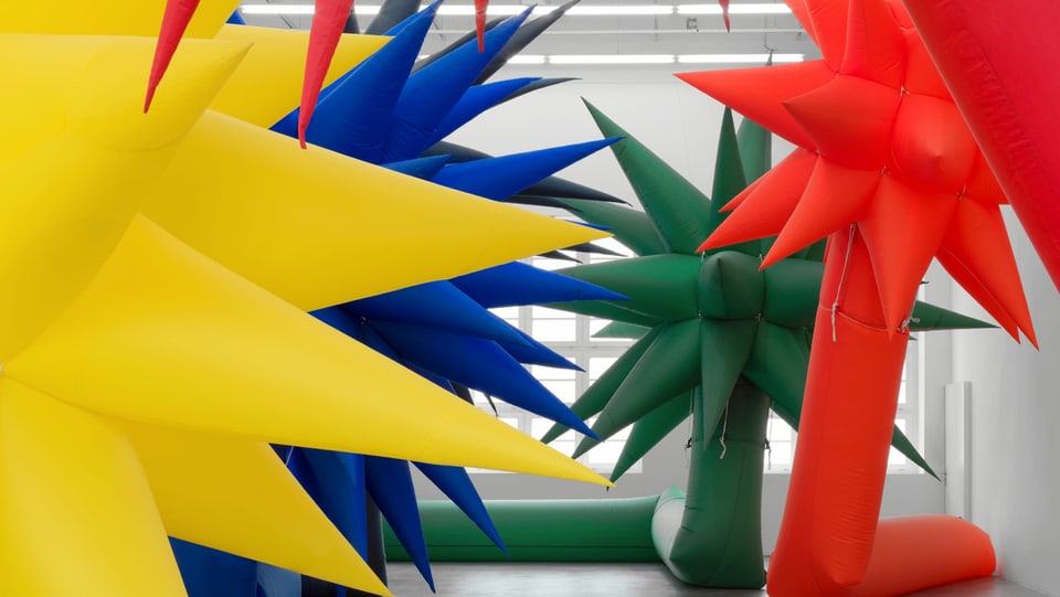 Riesige bunte aufblasbare palmenförmige Skulpturen in einer Ausstellungshalle.