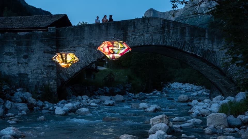 dunkler Fluss, vor Steinbrücke zwei farbenfrohe, leuchtende Lampions.