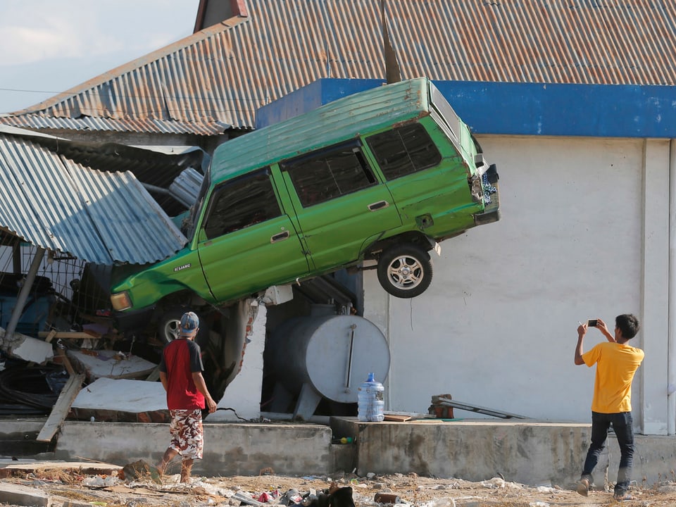 Grünes Auto, welches durch den Tsunami auf eine Mauer gehieft wurde.