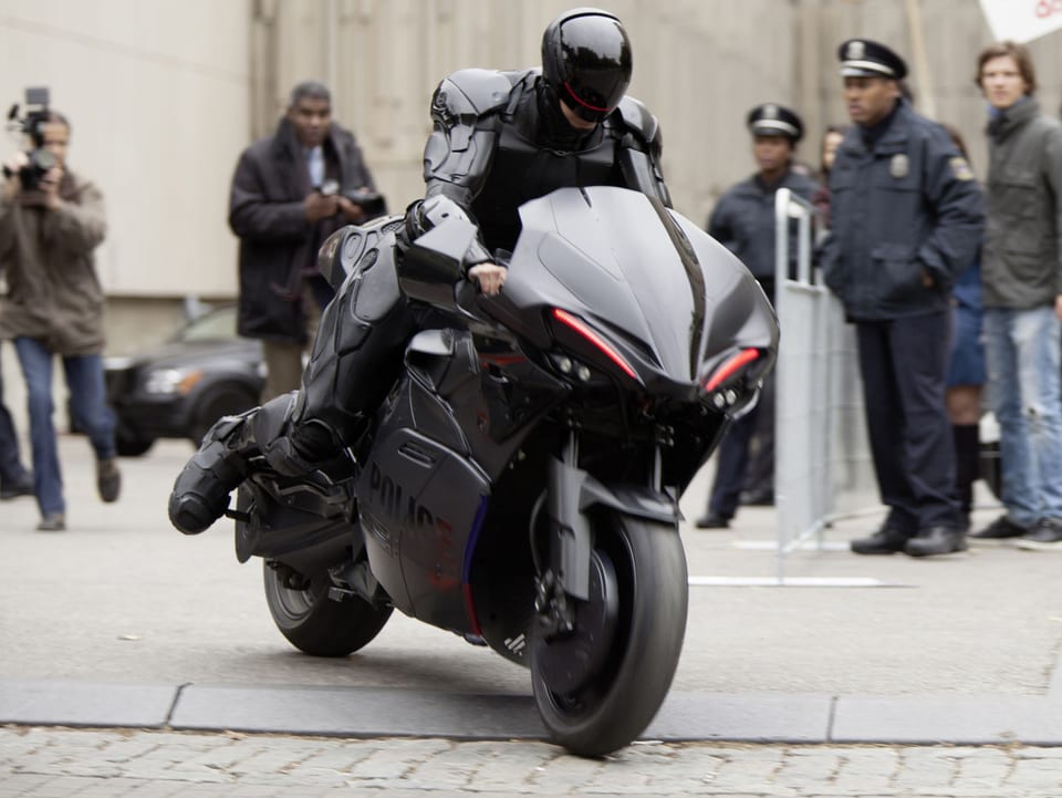 Robocop sitzt in Rüstung auf einem Motorrad.