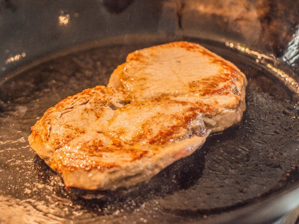 In einer Gusseisenpfanne wird ein Stück Fleisch angebraten. 