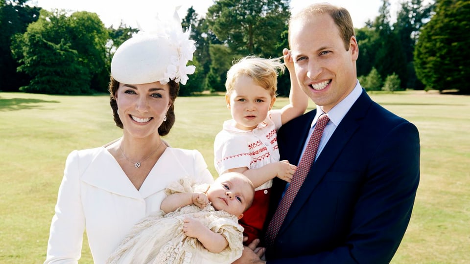 Kate, William, Charlotte und George auf einer Wiese stehend und in die Kamera lächelnd.