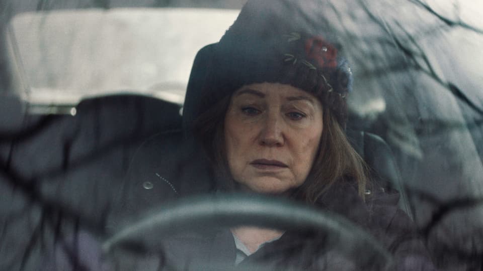 Eine Frau mit traurigem Gesicht sitzt in Winterkleidung im Auto.